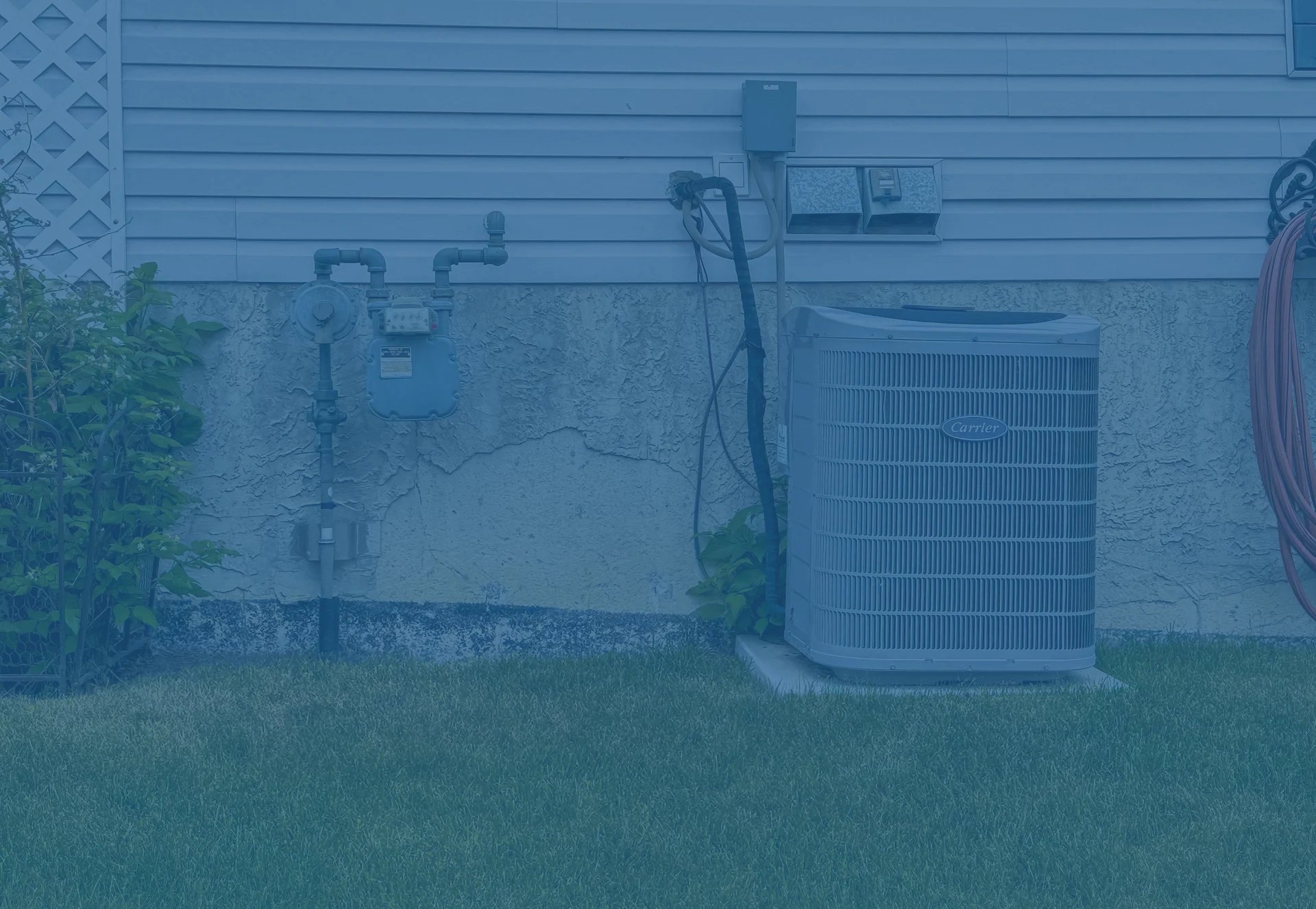 HVAC air conditioning unit installed outside a residential building with various mechanical components and piping visible against a blue siding wall